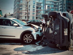 Two drivers are exchanging information beside their parked, slightly damaged vehicles on a tree-lined suburban street.